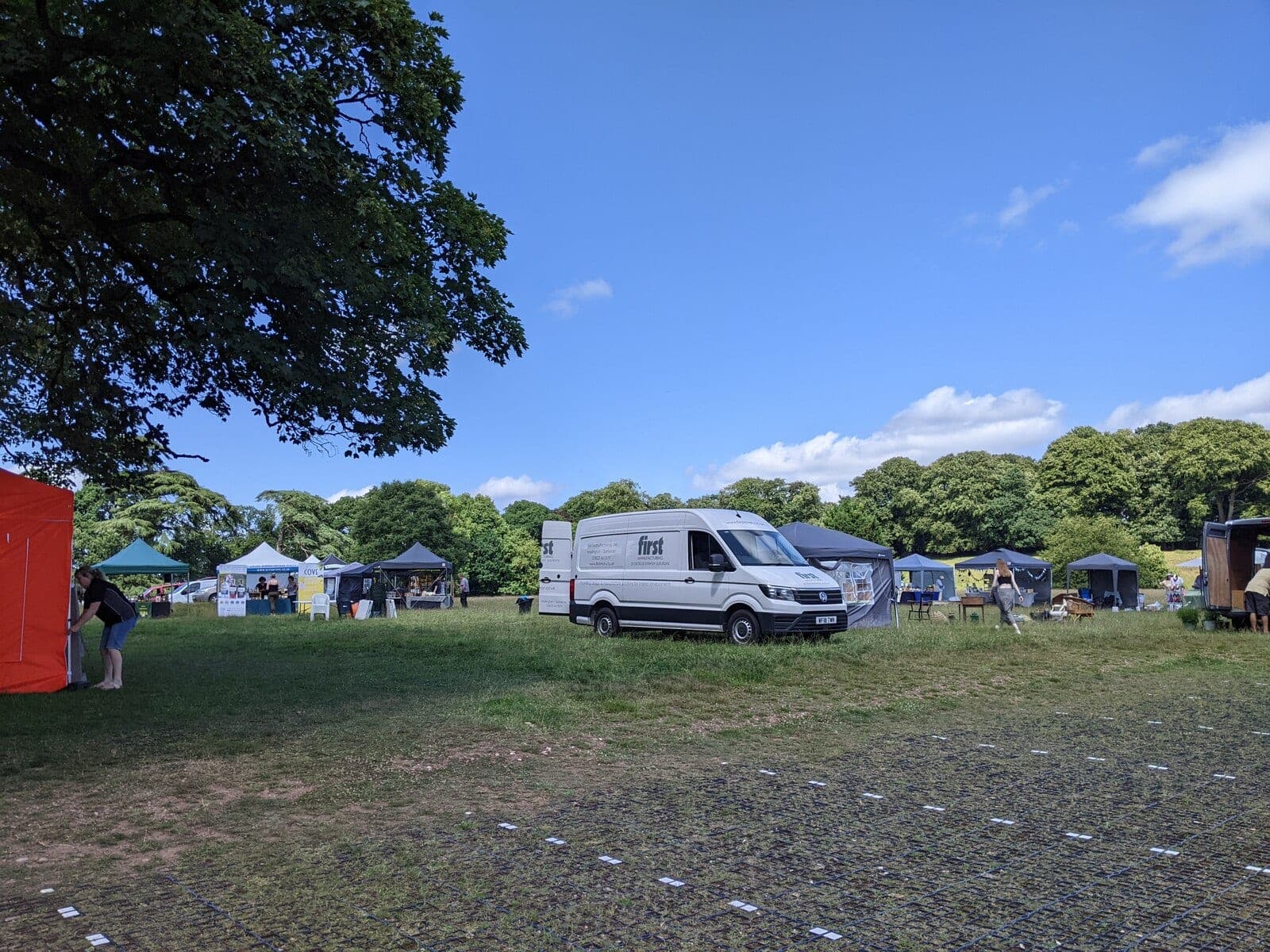 Traders setting up gazebo stalls on grass at an outdoor craft fair at Bridwell Park, with a van parked alongside