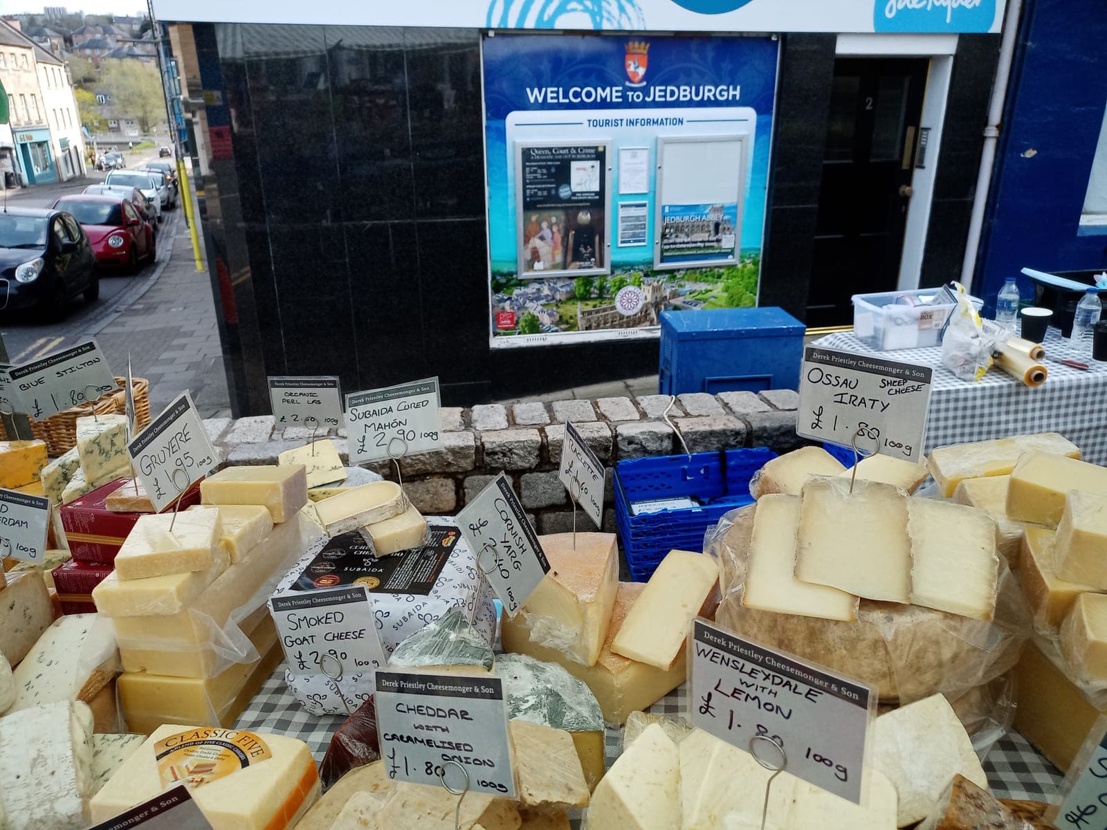 A stallholder standing behind a cheese stall stacked with produce at Jedburgh Easter Market in the Scottish Borders.