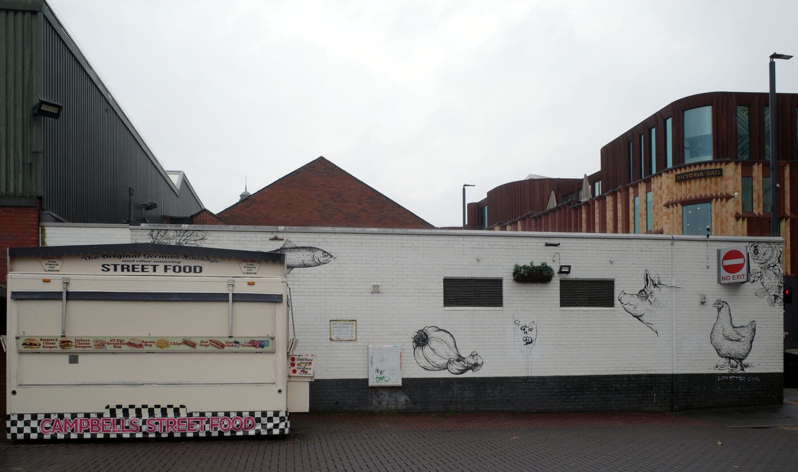 A street food trailer signed Campbells Street Food beside a white brick wall painted with line drawings of a pig, a chicken and a fish, Leeds Open Market.